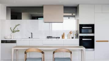 A modern kitchen with white cabinetry, a built-in oven, and a dining area with two wooden chairs.