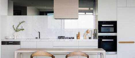 A modern kitchen with white cabinetry, a built-in oven, and a dining area with two wooden chairs.