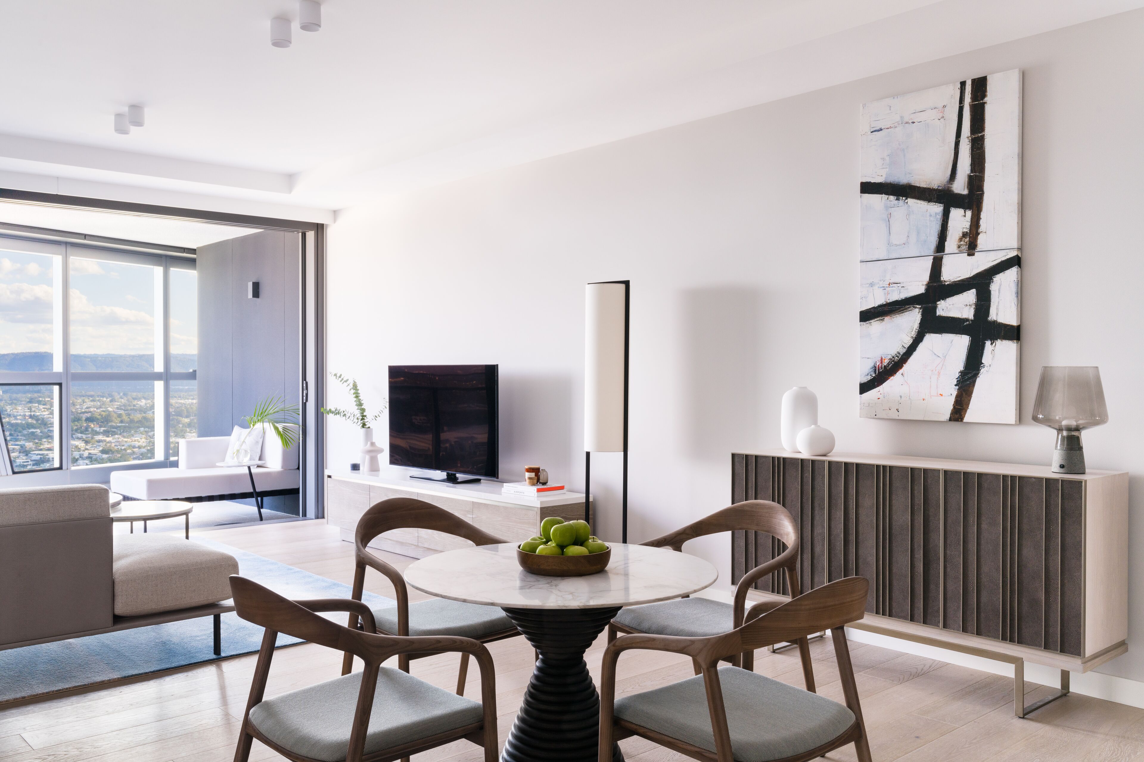 A modern living room with a round table, four chairs, a flat-screen TV, a painting, and a radiator.