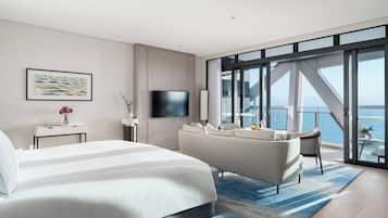 Ein modernes Hotelzimmer mit einem großen Bett, einer Sitzecke, einem Flachbildfernseher und einem Balkon mit Meerblick.