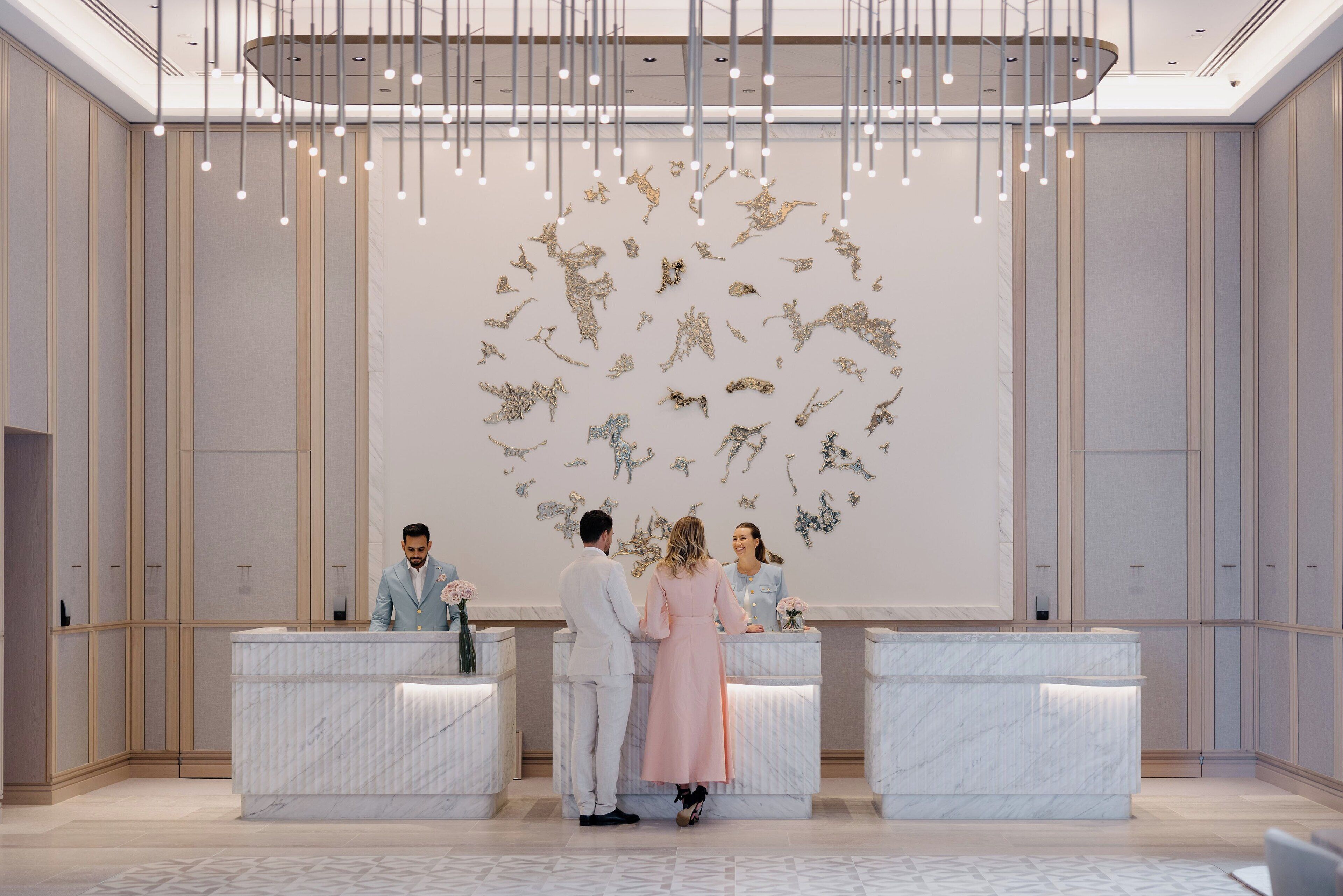 A reception area with marble counters, a modern chandelier, and a wall art installation.