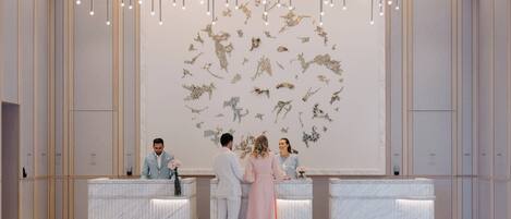 A reception area with marble counters, a modern chandelier, and a wall art installation.