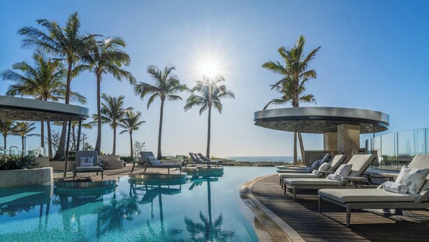 A pool area with lounge chairs and palm trees, surrounded by a wooden deck and a glass balustrade. - The Langham, Gold Coast and Jewel Residences (Surfers Paradise)