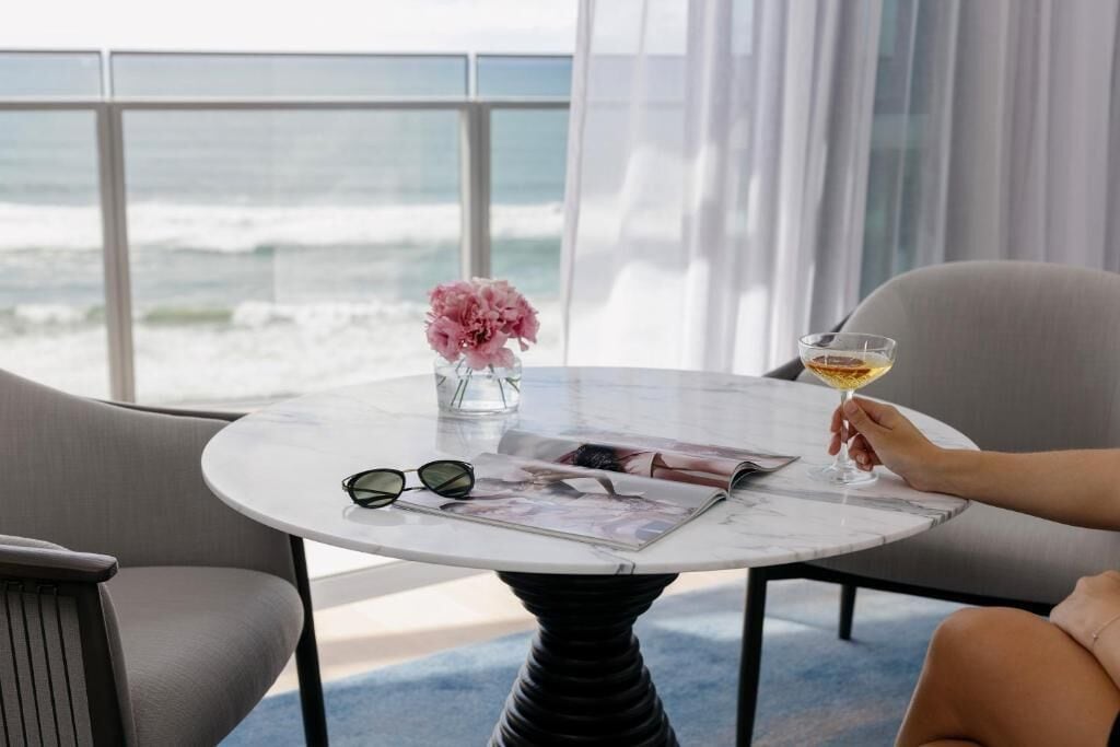 A round table with a magazine, a vase with pink flowers, and a glass of wine.