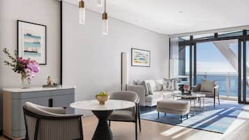 Un salon moderne avec un canapé, des fauteuils, une table basse et une vue sur l’océan grâce à de grandes fenêtres.