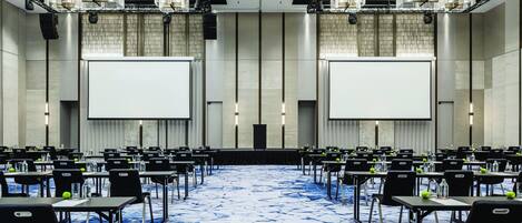 Une salle de conférence avec des rangées de tables, des chaises et un grand écran à l’avant.