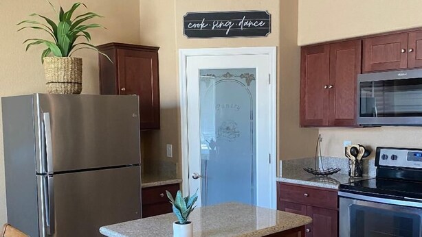 Eine Küche mit einem Edelstahlkühlschrank, einer Mikrowelle, einem Backofen und einem Holzkasten mit dem Schriftzug "cook sing dance".