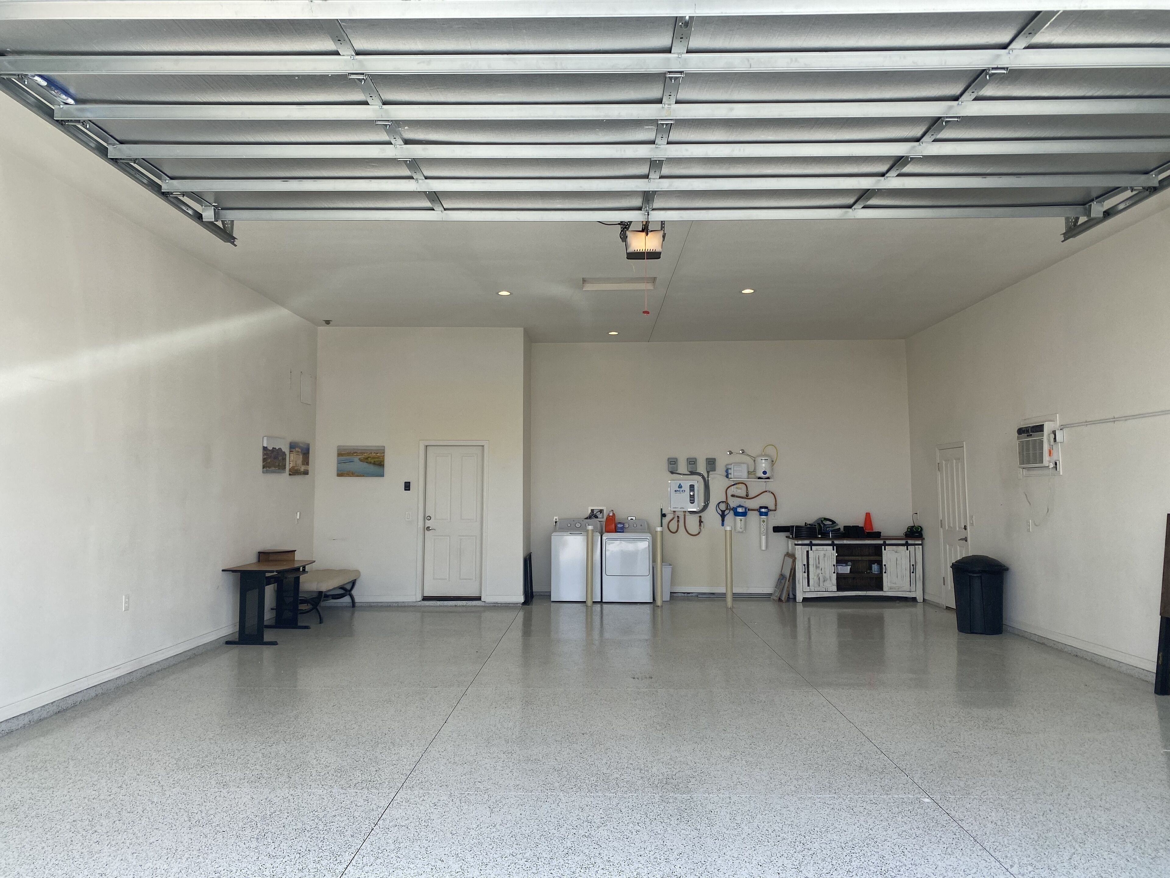 A spacious garage with a clean, white interior, a door, a refrigerator, and a wall-mounted air conditioning unit.