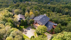 A large house with a spacious deck, surrounded by dense forest.