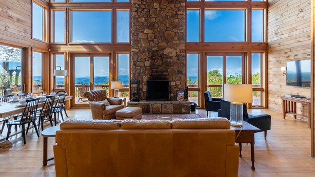 A spacious living room with a stone fireplace, large windows, and a view of the mountains. - Skytop Chateau at The Summit of Beech - Incredible 50+ Views! Game Room! (Beech Mountain)