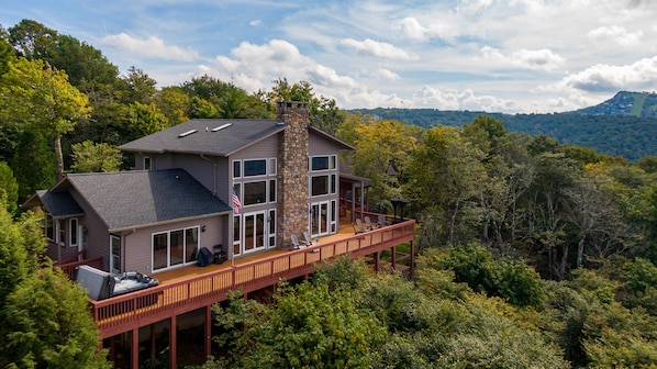 A two-story house with a stone chimney, large windows, and a deck with outdoor seating.