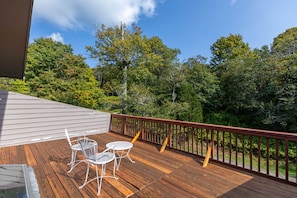 A wooden deck with a railing, two white metal chairs, and a glass table.