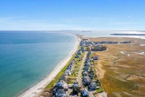 Vista aérea de una zona residencial costera con casas alineadas a lo largo de una playa, un cielo despejado y un mar tranquilo.