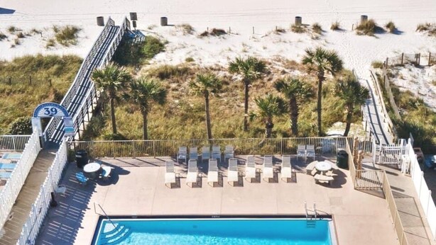 Zona de piscina frente al mar, con vista despejada al océano, una playa arenosa y un camino que lleva a la piscina.