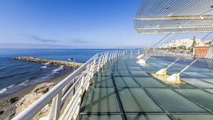 A glass bridge with metal railings overlooking a beach and ocean. - A&n Torrox Beach    . (Torrox Costa)