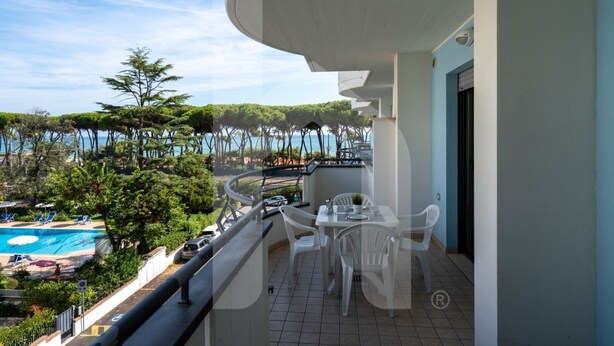 Un balcon avec vue sur la piscine, des chaises blanches et une table.