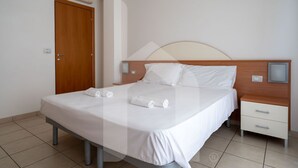 Un lit bien fait, avec du linge de lit et des serviettes blanches, une tête de lit en bois, une table de chevet avec une lampe et une porte en bois.