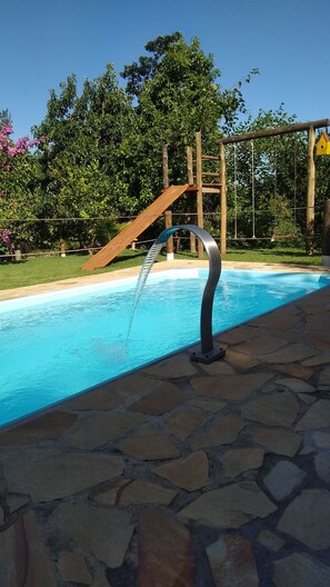 A swimming pool with a water feature, surrounded by a stone deck and a wooden play structure. - A location surrounded by nature, offering tranquility and peace, close to the center (Louveira)