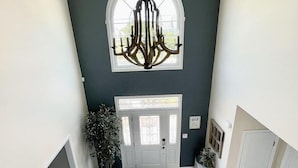 A spacious entryway with a grand chandelier, a large arched window, and a white door with a glass panel. - 5BR/3BTH waterfront family beach house with hot tub, kayaks, bikes and game room (Mantoloking)