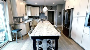 A modern kitchen with a central island, stainless steel appliances, and white cabinetry. - 5BR/3BTH waterfront family beach house with hot tub, kayaks, bikes and game room (Mantoloking)