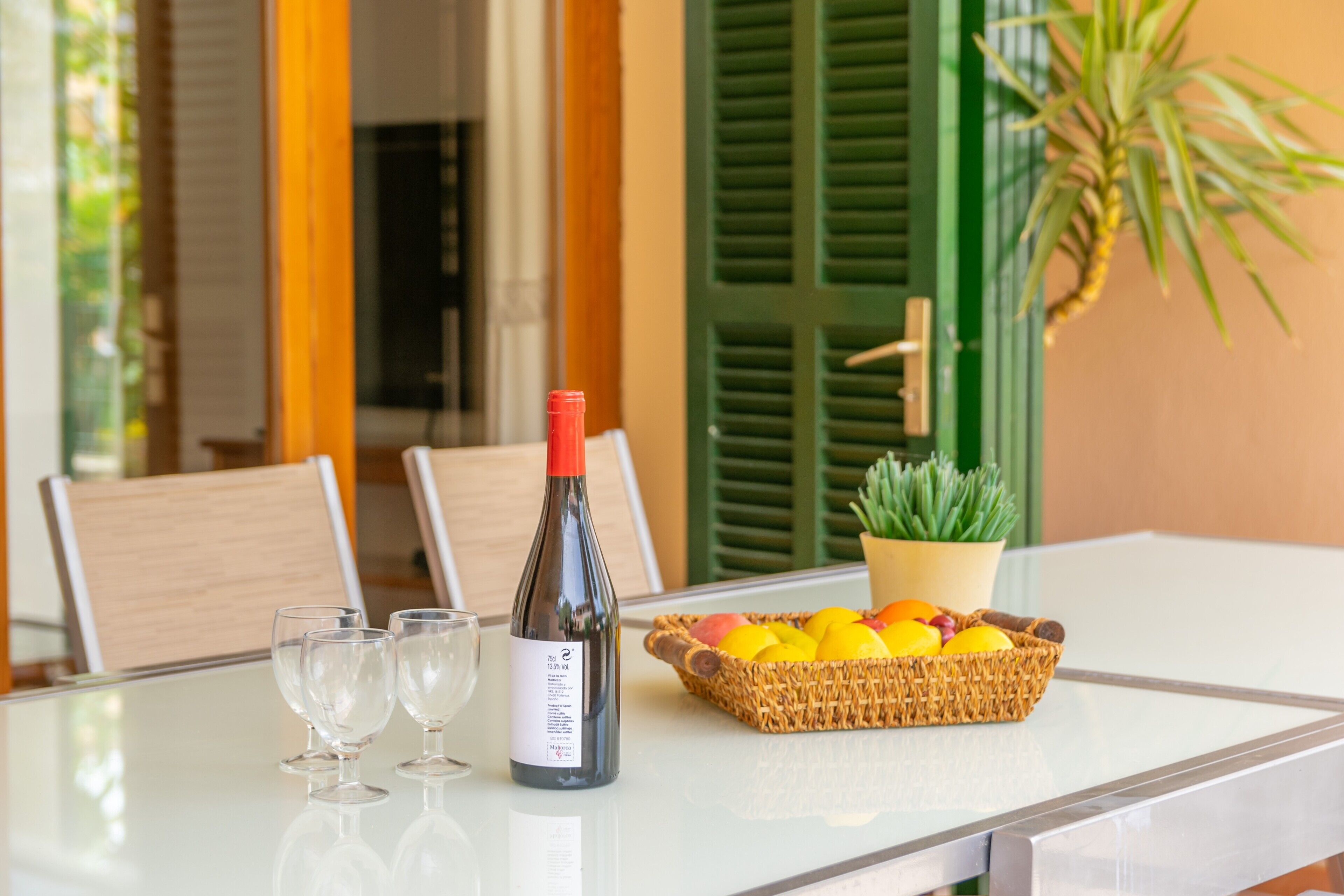 A table with a bottle of wine, two glasses, and a basket of fruit.