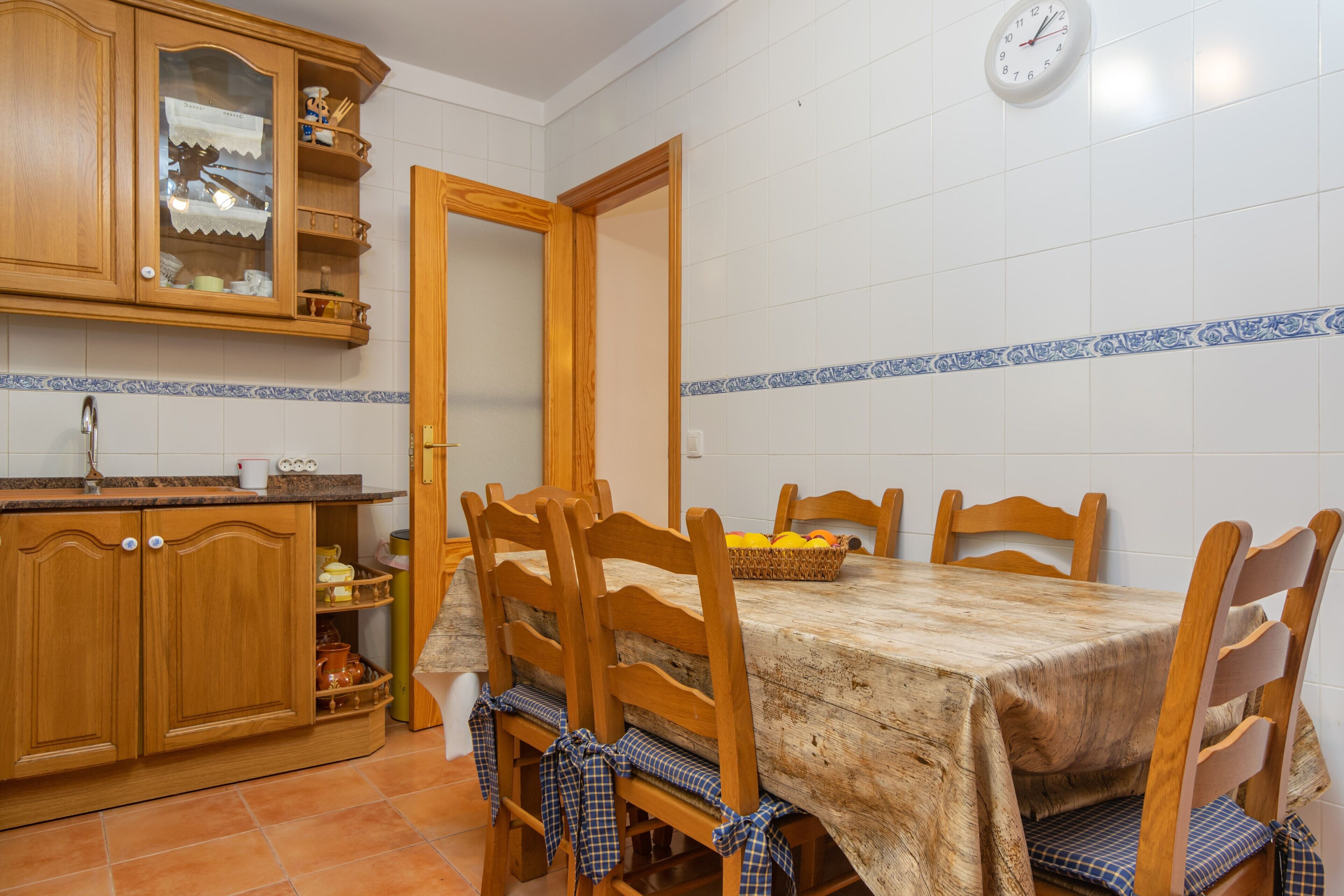 Un coin repas avec une table et des chaises en bois, une cuisine avec des placards en bois et une horloge au mur.