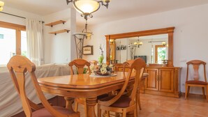 Zona pranzo con tavolo e sedie in legno, un lampadario e un grande specchio sopra il tavolo.