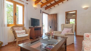 Una sala de estar con techo de madera, muebles de mimbre, una mesa de centro de vidrio y un televisor.