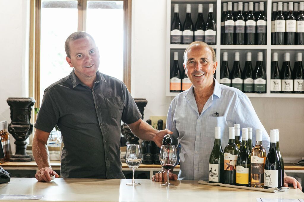 Two individuals at a bar with wine bottles and glasses.