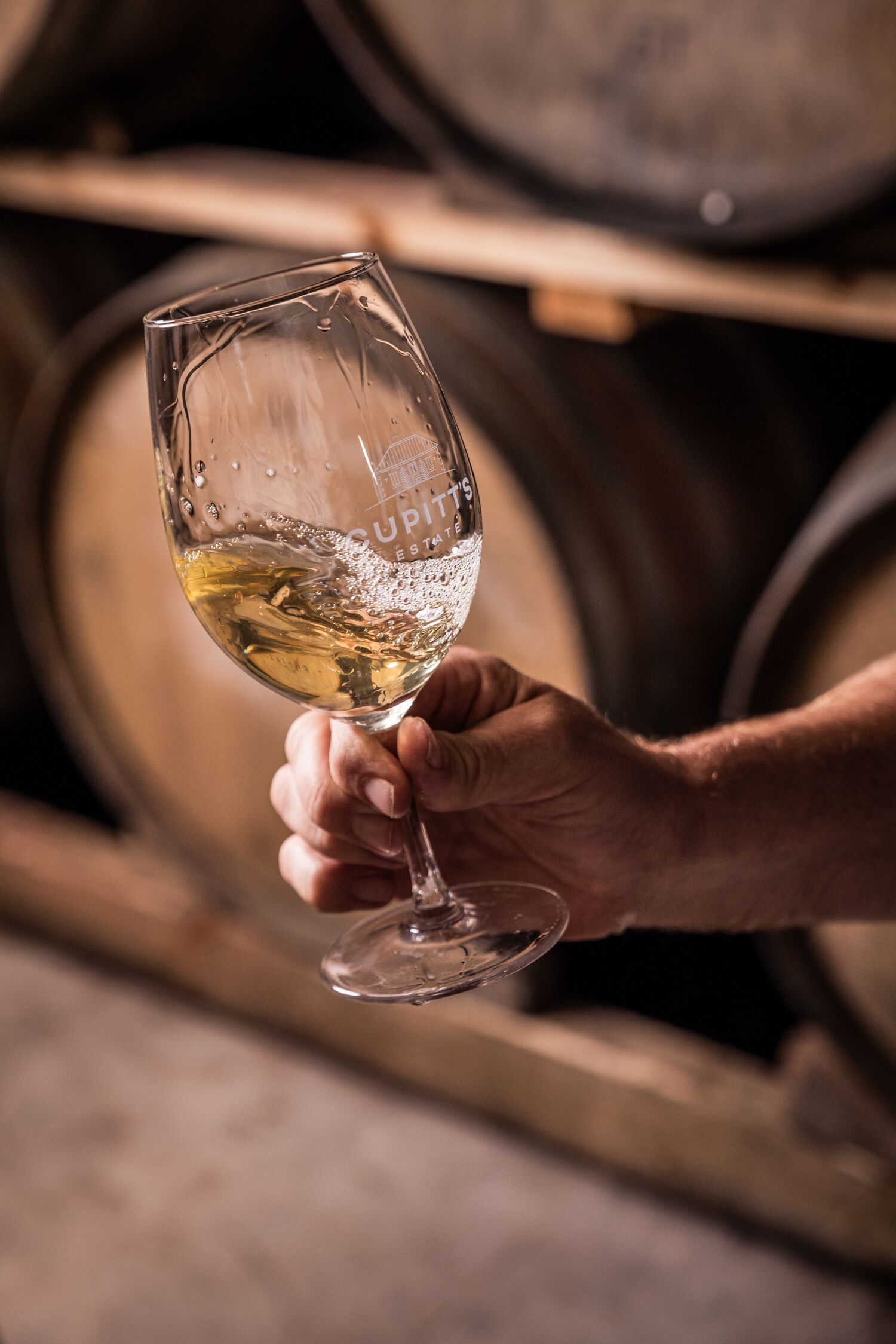 A hand holding a wine glass with a label that reads "CUPITS ESTATE 1744".