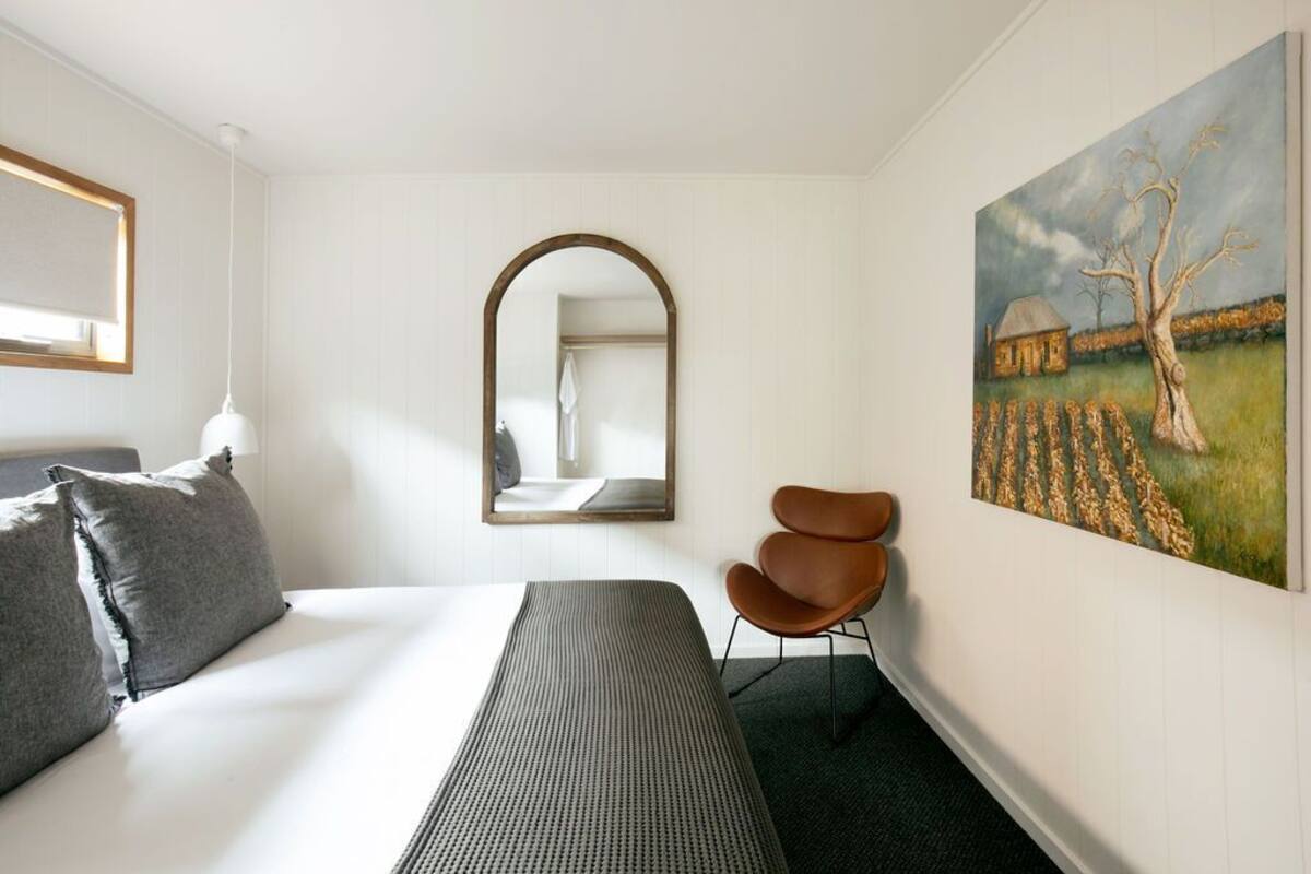A hotel room with a bed, a mirror, a chair, and a painting on the wall.