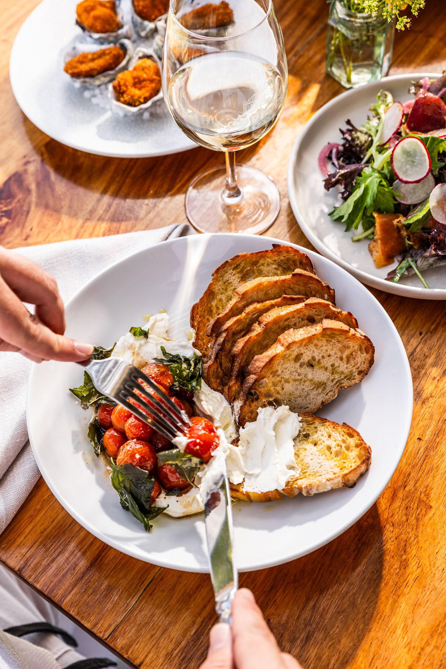 A dining table with a plate of food, a glass of white wine, and a salad.