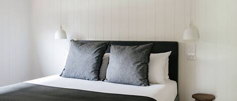 A modern bedroom with a bed, two bedside lamps, a small stool, and a white wall with vertical paneling.
