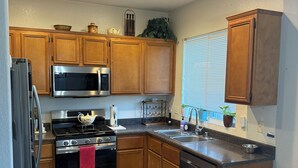 A kitchen with wooden cabinets, stainless steel appliances, a herringbone-patterned floor, and a window with blinds. - Nice, & cool 4- bedroom home to enjoy a stay and relax in.  (Coachella)