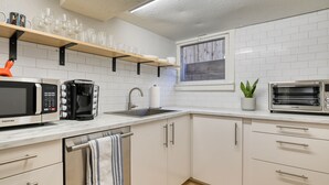 Una cocina moderna con armarios blancos, microondas de acero inoxidable, cafetera, pileta y horno tostador.
