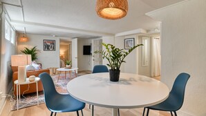 Una sala de estar moderna con una mesa redonda blanca, sillas azules, una lámpara colgante de fibras tejidas y una planta en maceta.