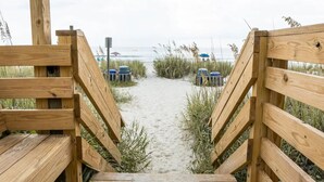 Een houten pad dat naar een strand met zand en gras leidt, met uitzicht op de oceaan.