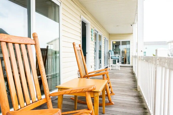A wooden deck with chairs and tables, a white fence, and a building with large windows and doors.