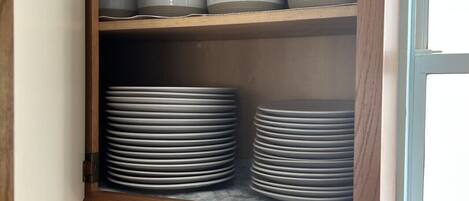 A kitchen with a wooden cabinet containing stacked plates and bowls.