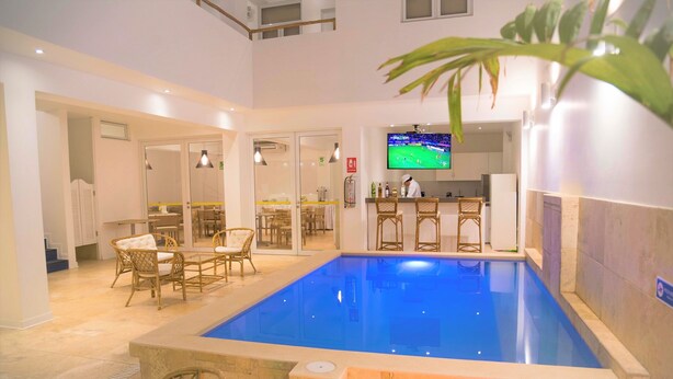 A hotel with a swimming pool, wicker furniture, a bar area, and a television screen.