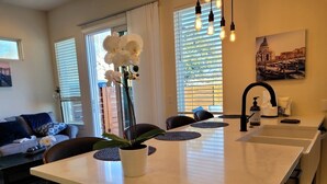 A modern kitchen with a central island, a dining area with a sofa and chairs, and a view of the outside through large windows.