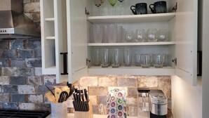 A kitchen with a brick backsplash, a built-in cabinet with glassware, a coffee maker, and a utensil holder.