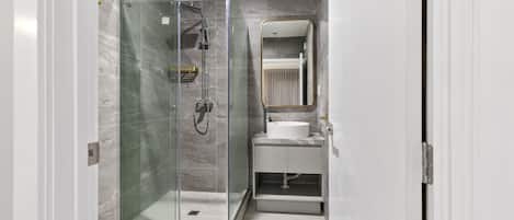 Un baño moderno con cabina de ducha de vidrio, lavamanos blanco y espejo con marco dorado.