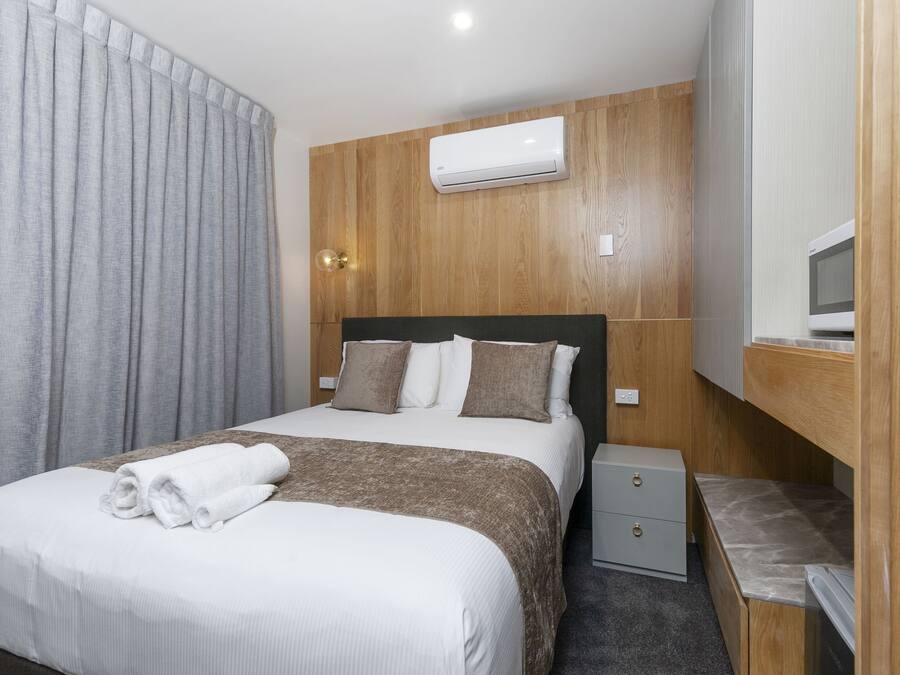 Una habitación de hotel con cama, mesita de noche, armario y aire acondicionado.