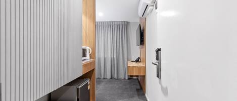 A compact hotel room with a kitchenette, a small desk, a chair, a TV, and a sliding door.