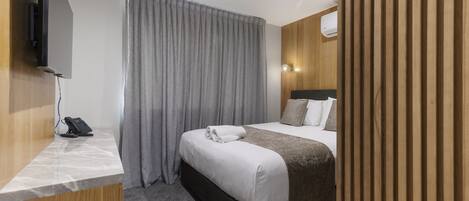 A hotel room with a bed, a desk with a phone, a TV, and a curtain.