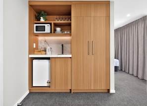 Een kleine keuken met een magnetron, koffiezetapparaat en opbergkasten.
