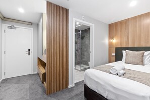 Una habitación de hotel moderna con una cama, un separador de madera, una zona de ducha y una puerta blanca.