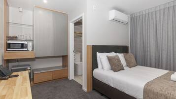 Una habitación de hotel moderna con cama, mesita de noche, microondas y una pequeña zona de estar con un banco.