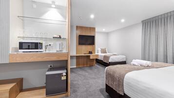 A modern hotel room with a microwave, refrigerator, flat-screen TV, two beds, and a glass coffee table.